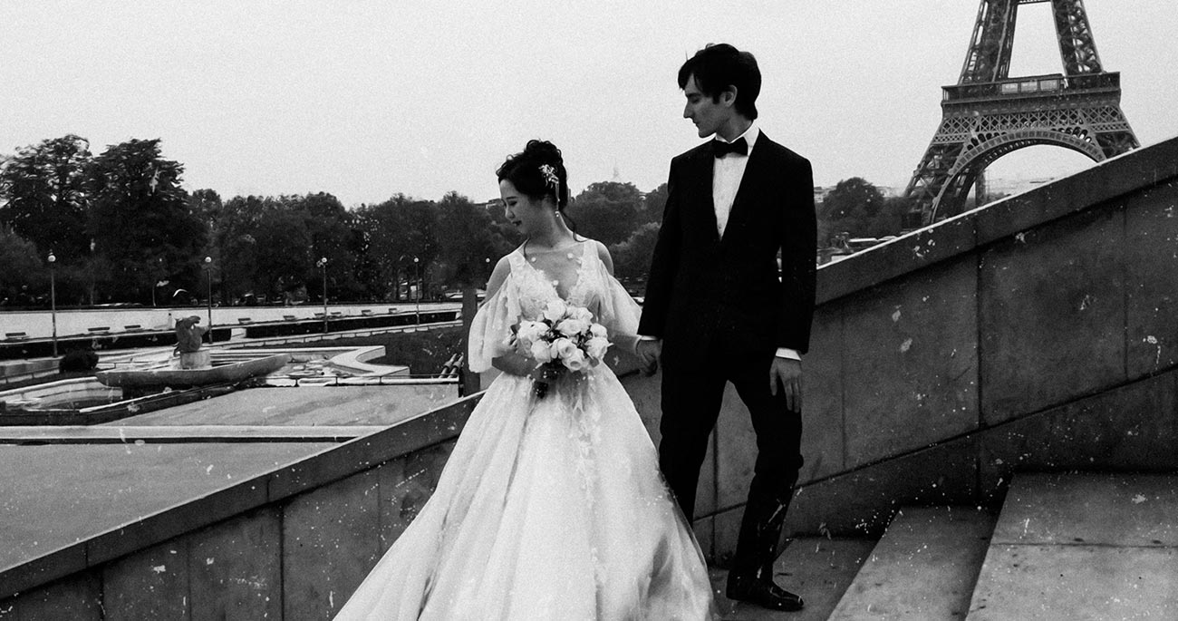 A man and woman in wedding attire standing on the side of a bridge.