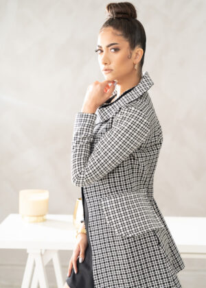 A woman in black and white checkered jacket standing next to table.