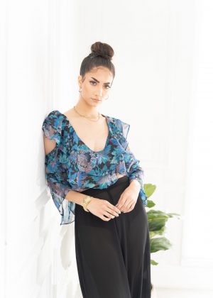 A woman in black pants and blue floral top.