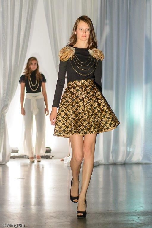 A woman in black shirt and skirt walking on runway.