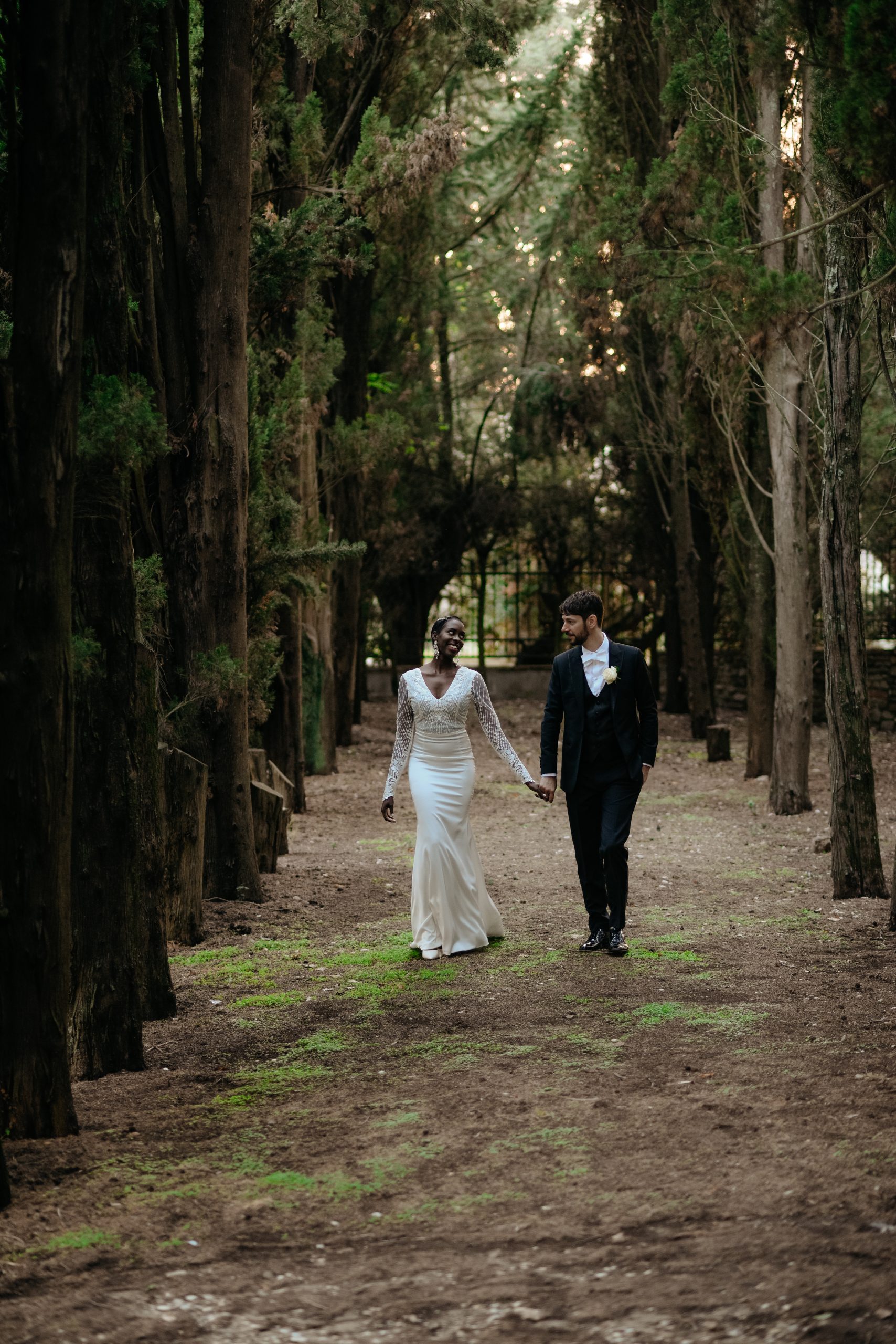 A man and woman walking through the woods holding hands.